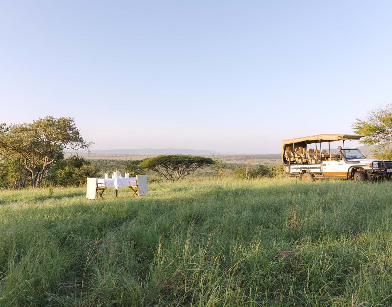 A couple eat breakfast in the grass near a parked rover