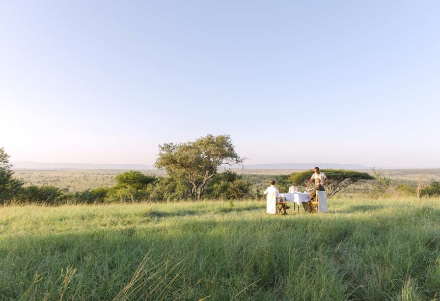 A man serving a couple breakfast in the grass