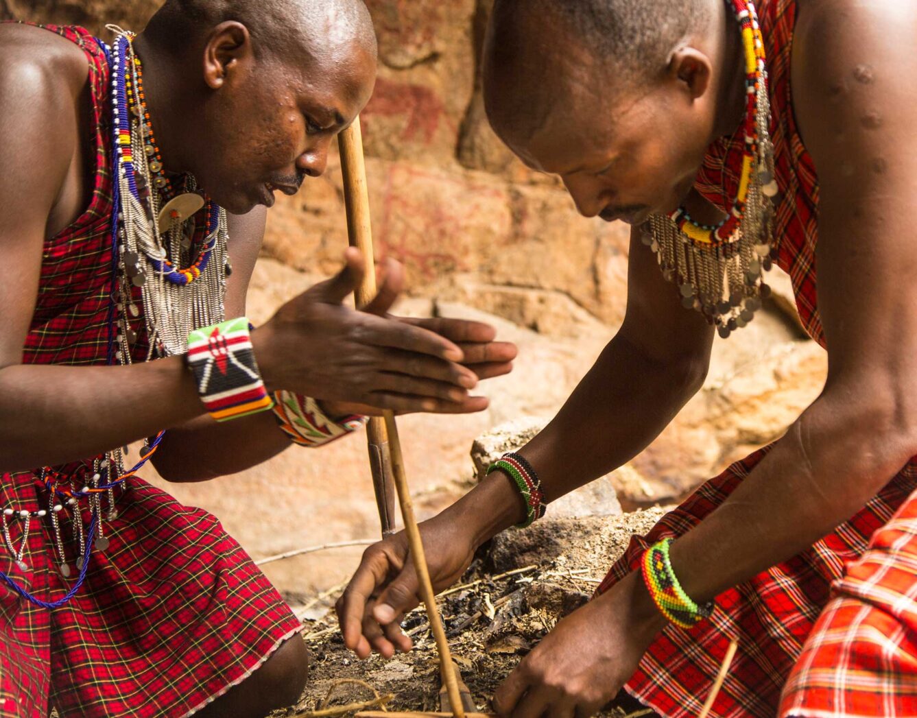 Two men rub sticks together to start a fire