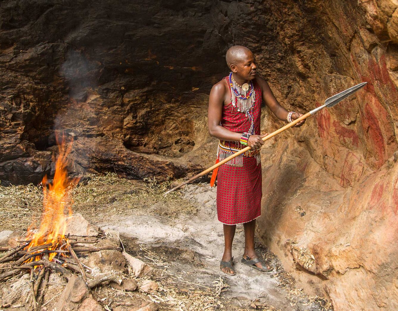 A man stands with a spear beside a fire