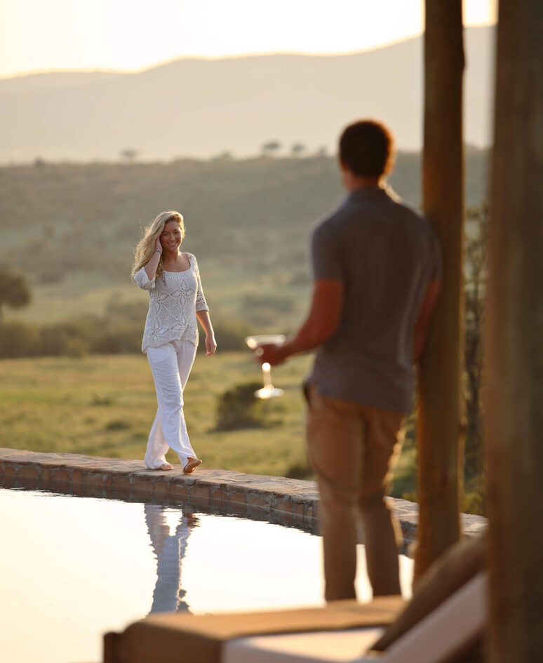 A man waits for a women as she walks along the side of the pool